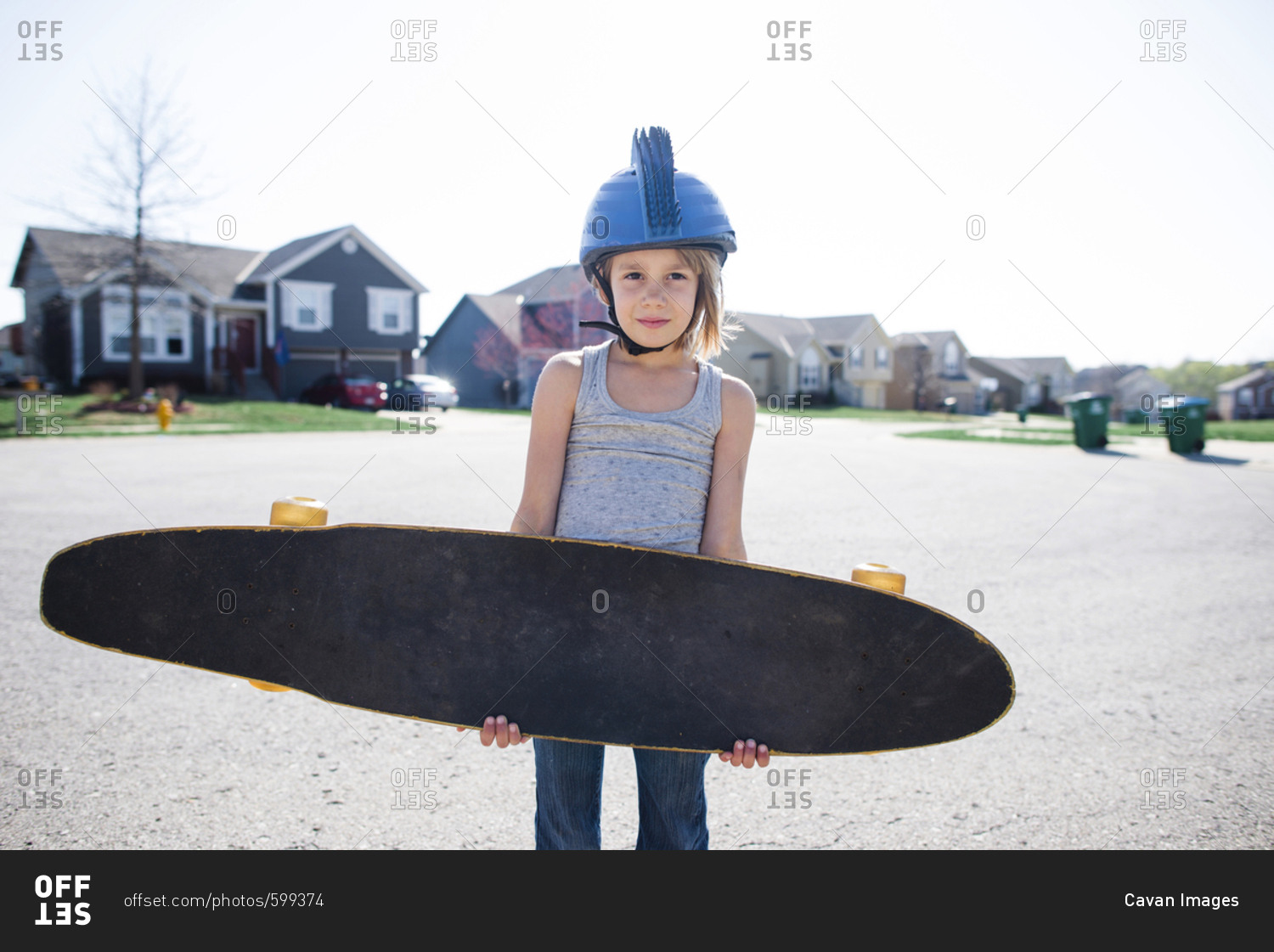 Portrait of girl in helmet carrying skateboard while standing on street during summer