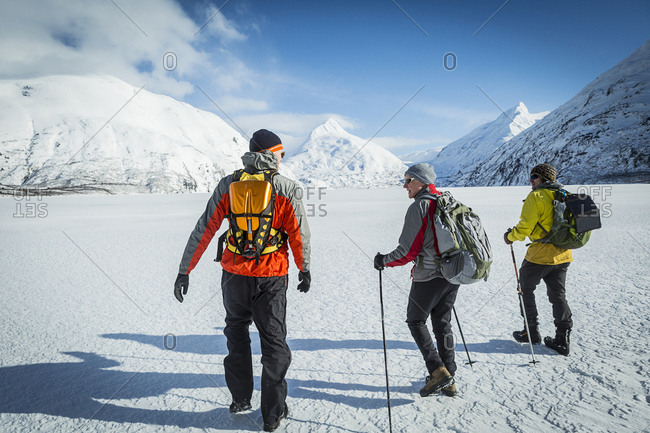 Father and two adult sons hiking away across a snow covered frozen lake