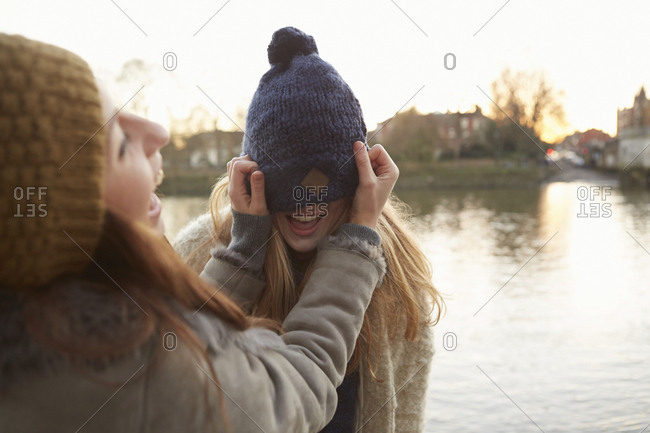 Young woman putting knitted hat on friend, hat covering eyes, laughing