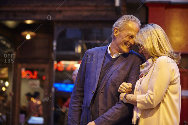 Mature dating couple arm in arm on city street at night, London, UK