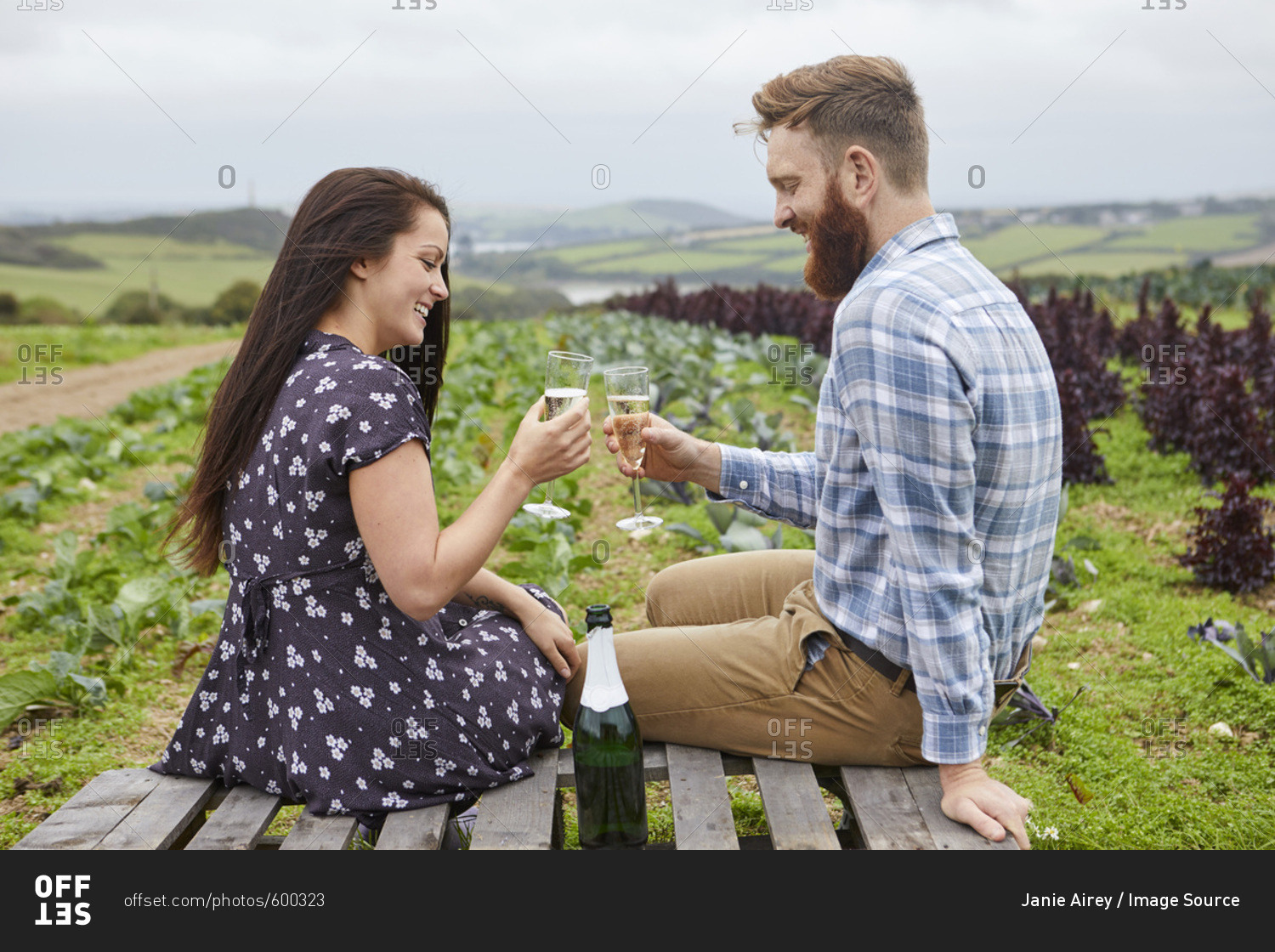 Couple in rural location sitting on pallets making a toast