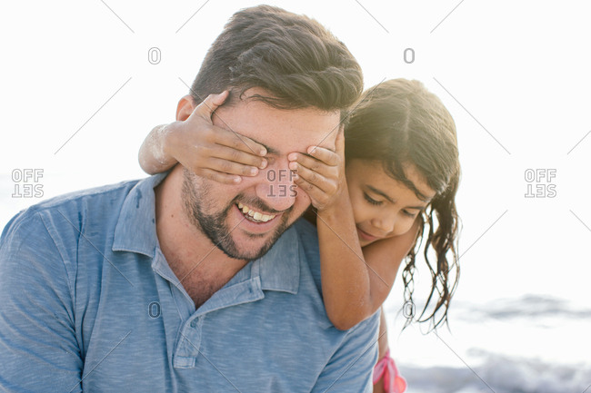 Girl with hands covering fathers eyes on beach, Tuscany, Italy