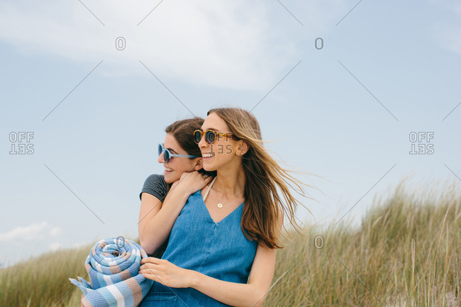 Two young female friends carrying picnic blanket on dunes