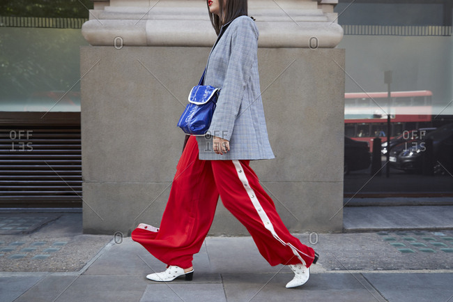 London, England - June 11, 2017: Woman in red trousers and grey jacket walking, side view