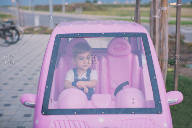 Little boy sitting in pink toy car