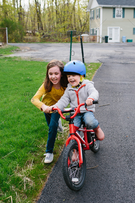 Girl helping her younger brother learn to ride a bike