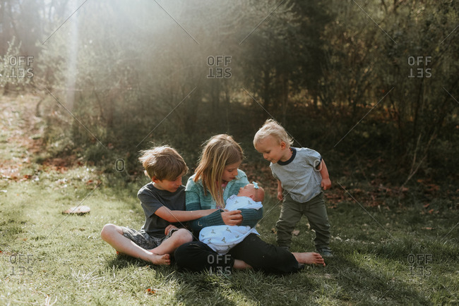 Children sitting with newborn sibling outdoors