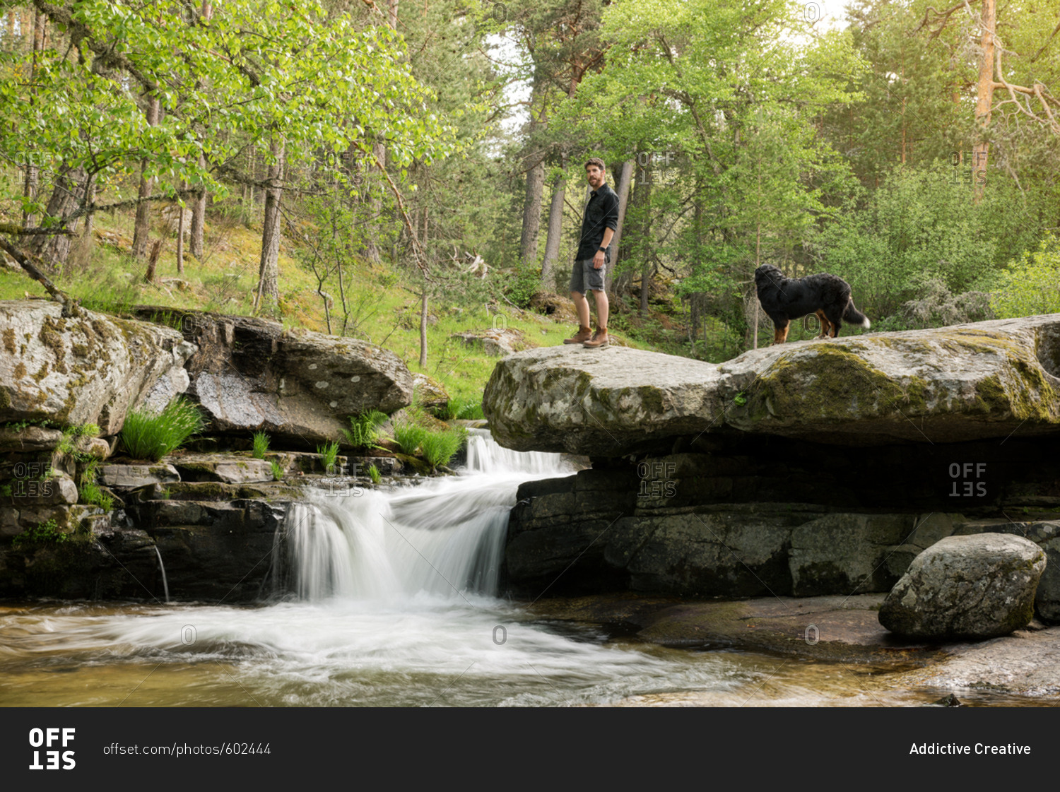 Young man enjoys rest at the waterfall after adventure with his dog
