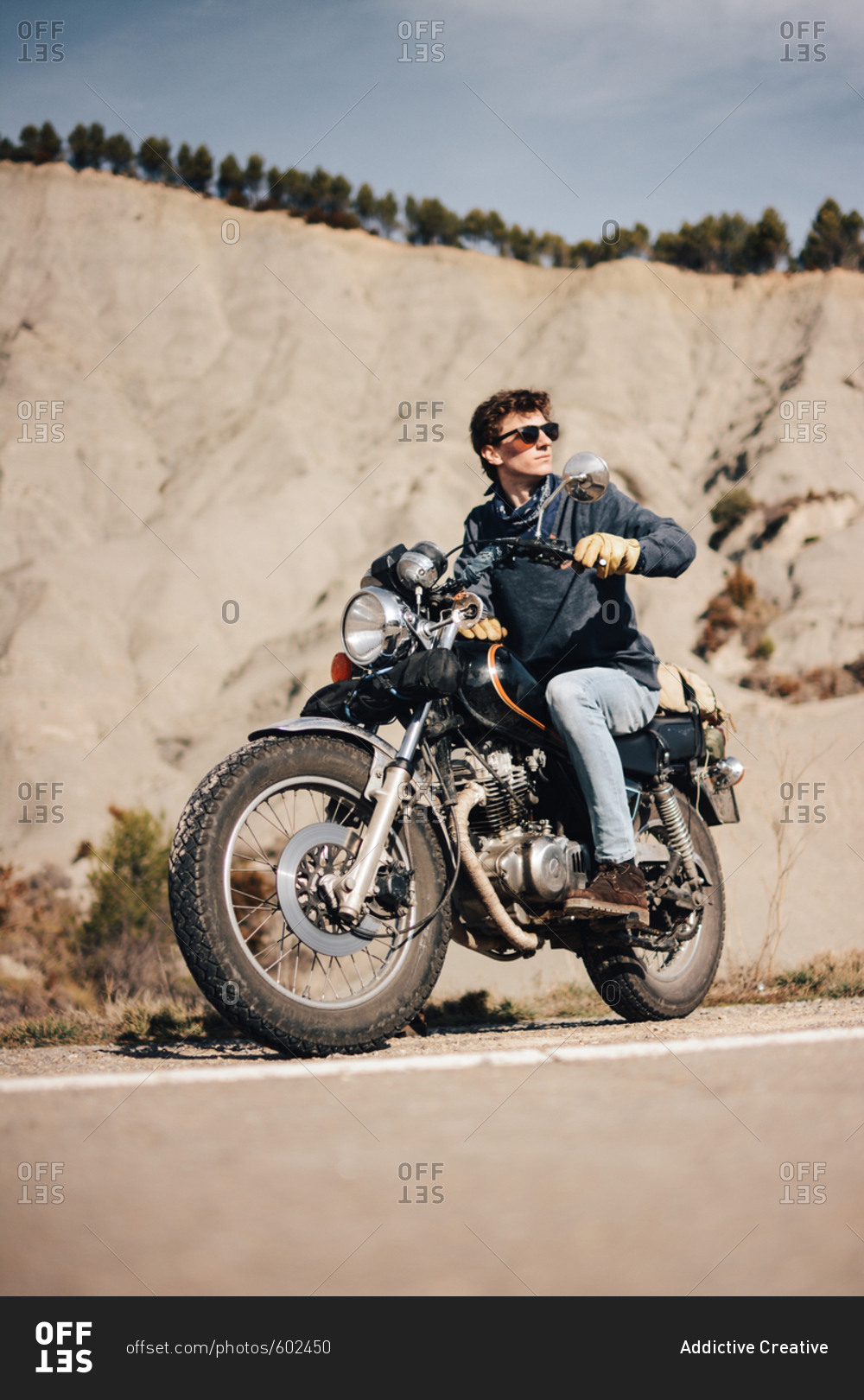 Cool young handsome man sitting on motorcycle and looking away on roadside