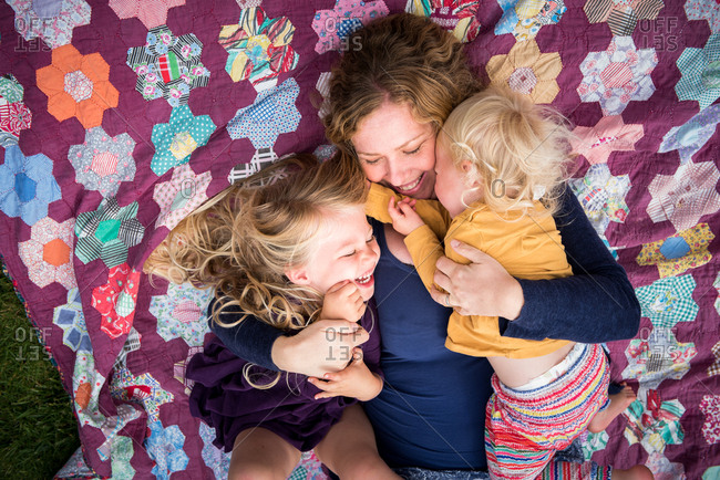 Overhead portrait of affectionate mother with two young daughters lying on quilt