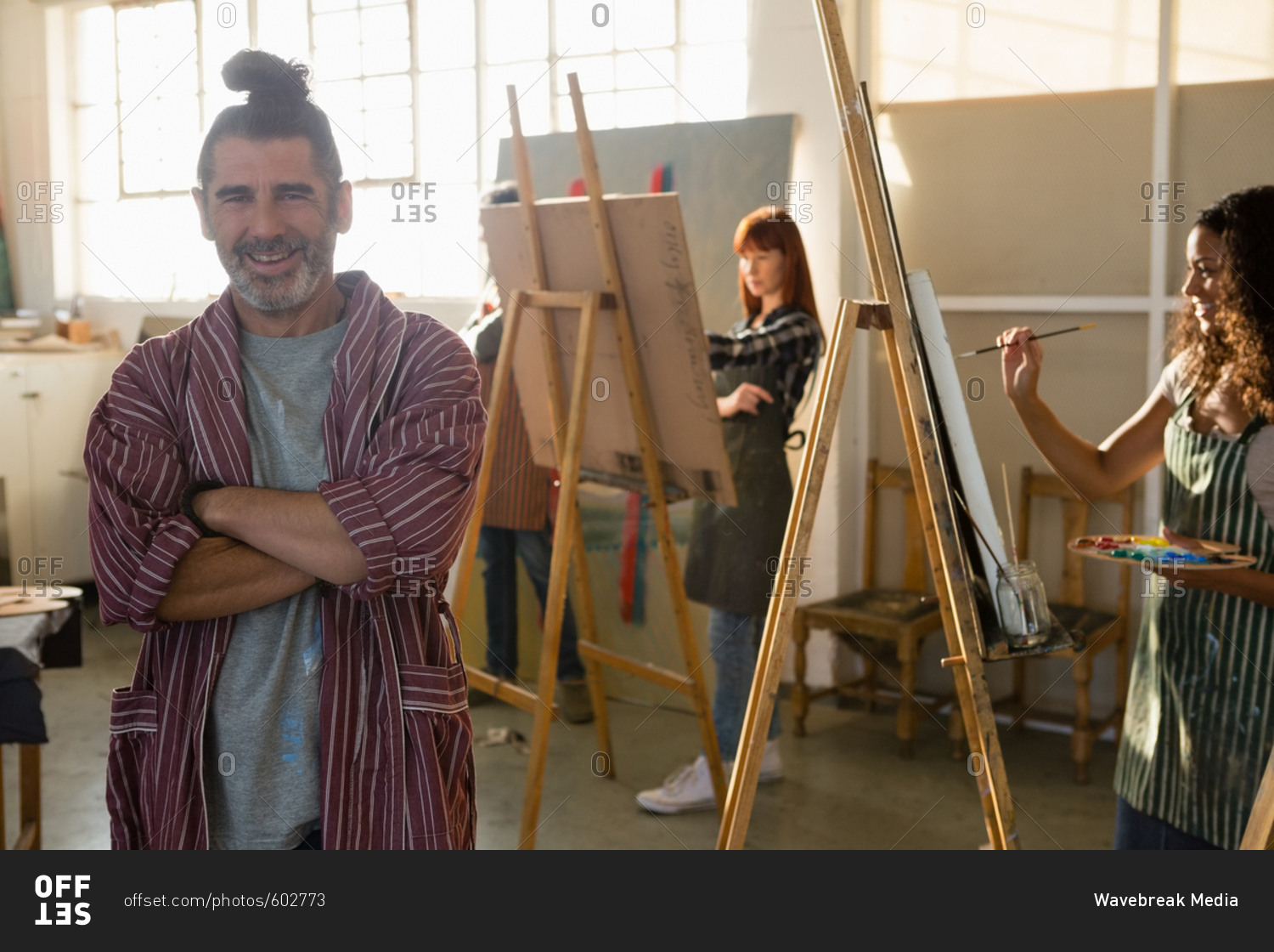 Portrait of smiling woman with arms crossed with friends painting in background at art class