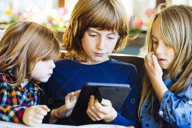 Brothers and sister with long blond hair using digital tablet together in restaurant