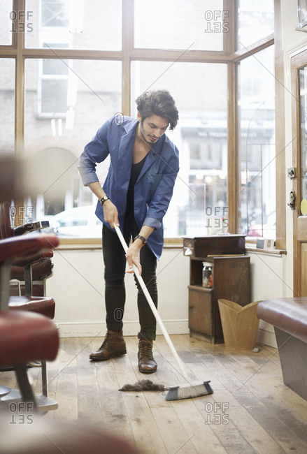 Man sweeping barbershop floor with broom