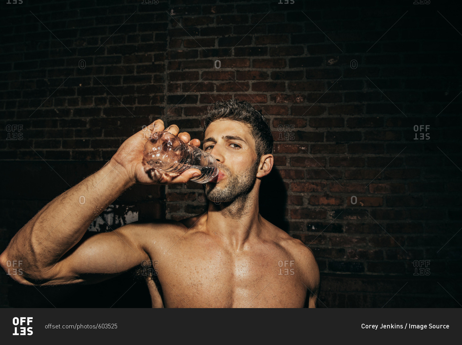 Portrait of bare chested young man drinking water on street at night