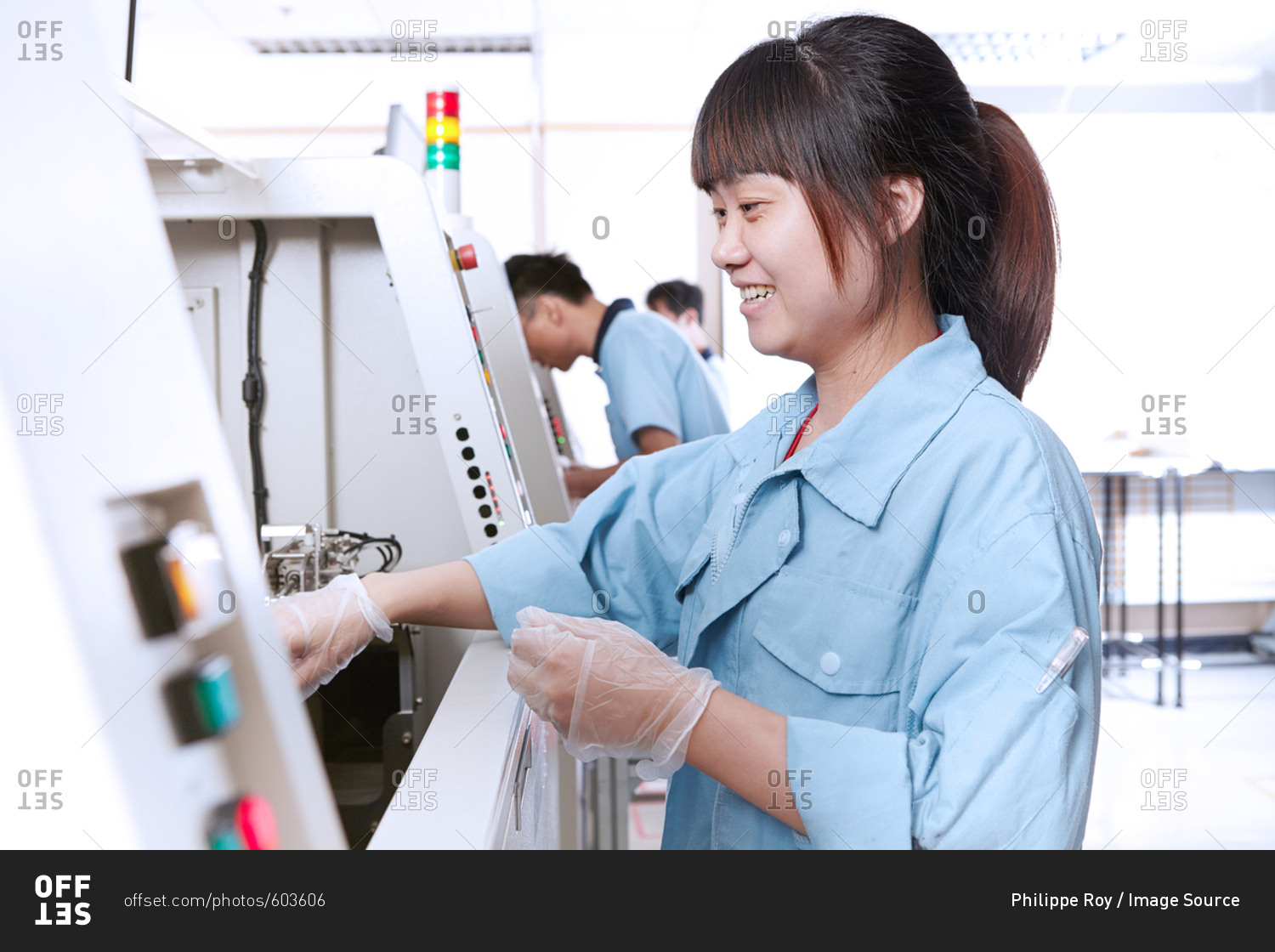 Young woman in flexible electronics plant using machine smiling