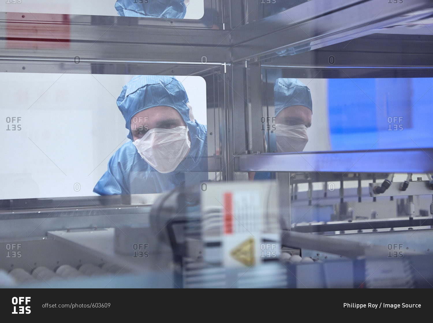Male worker looking through machine window in flexible electronics factory clean room