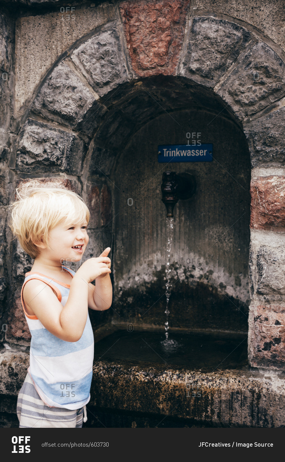 Side view of boy standing by stone drinking fountain, Bludenz, Vorarlberg, Austria