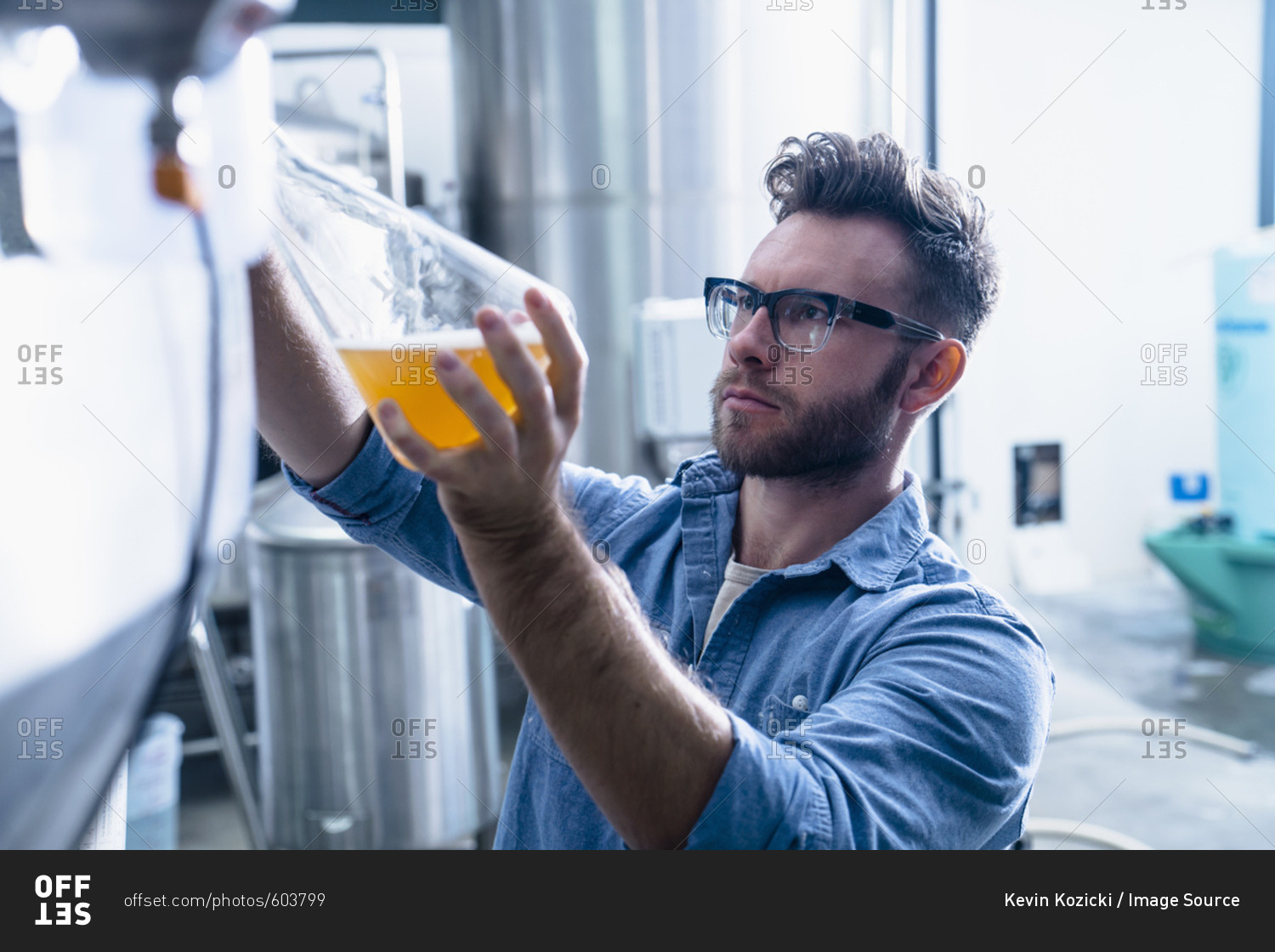 Young man in brewery filling flask with beer