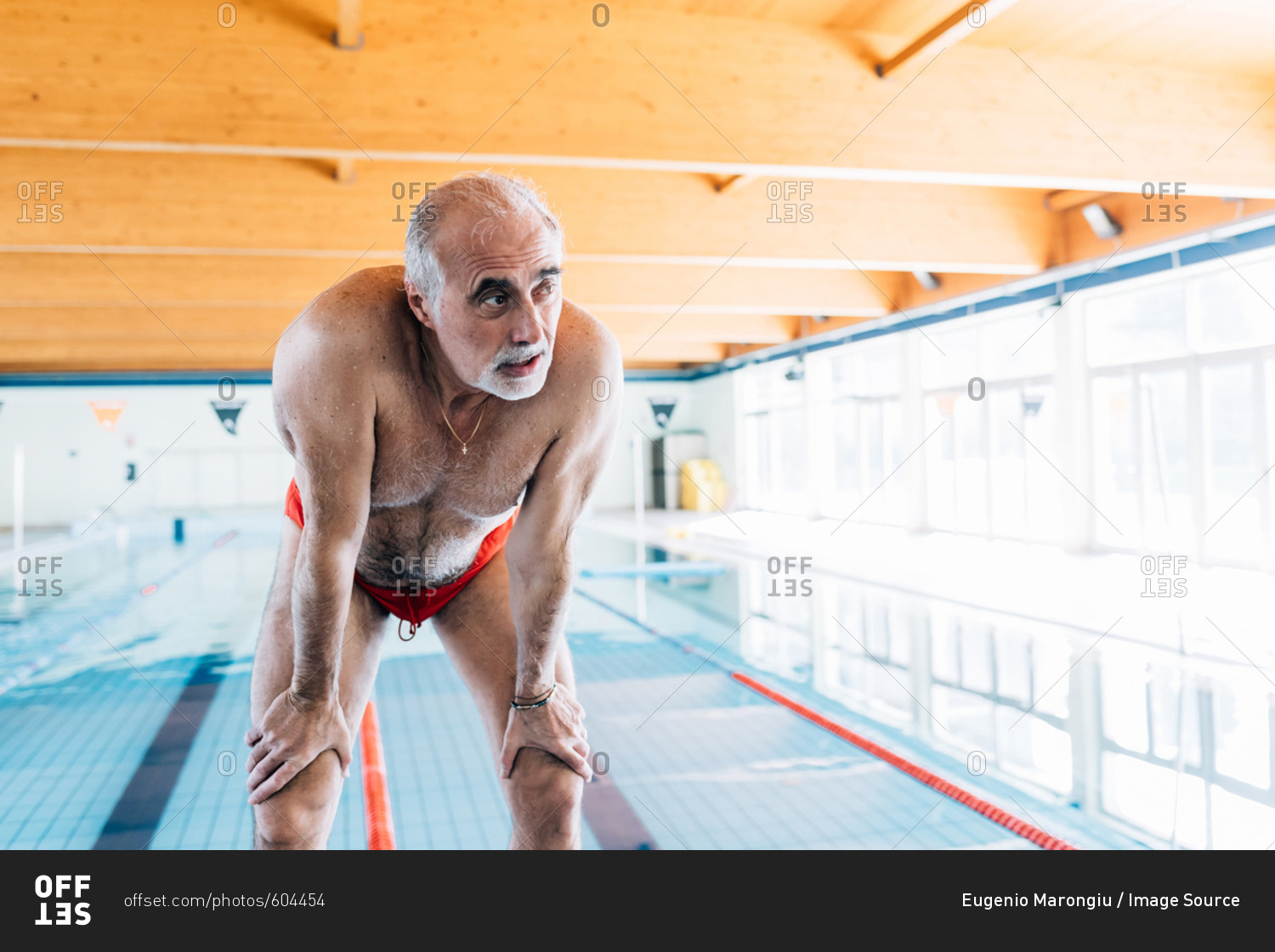 Senior man bending over catching his breathe by pool stock photo OFFSET