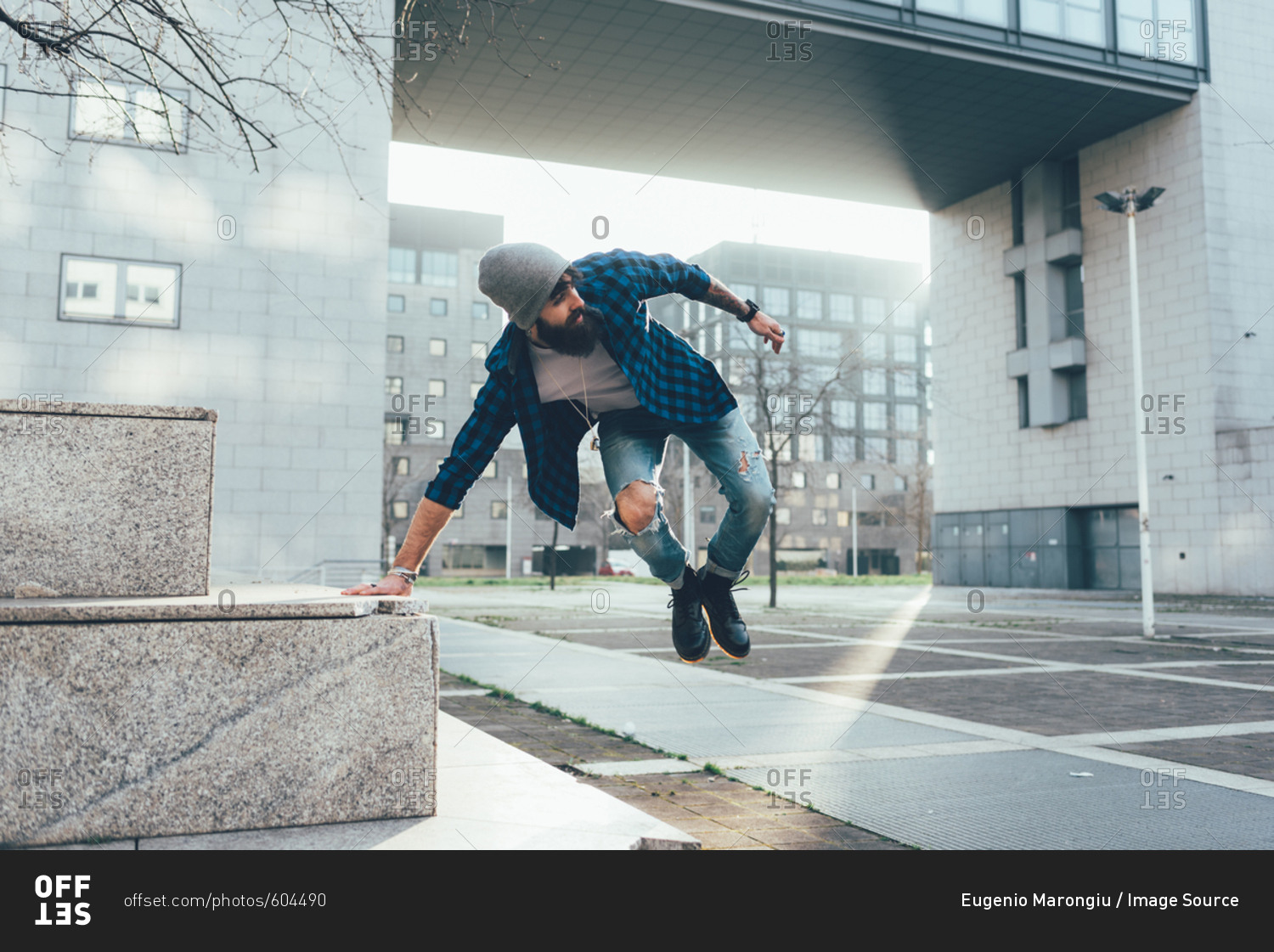 Young male hipster jumping mid air practicing parkour in city