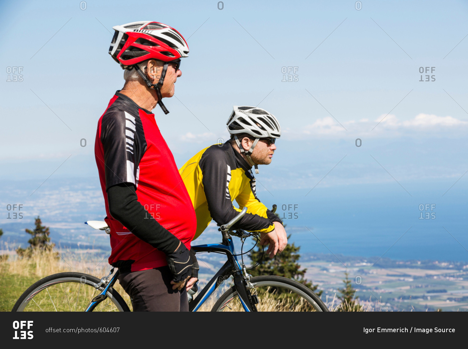 Senior man and grandson, wearing cycling clothes, standing on hill, looking at view, Geneva, Switzerland, Europe