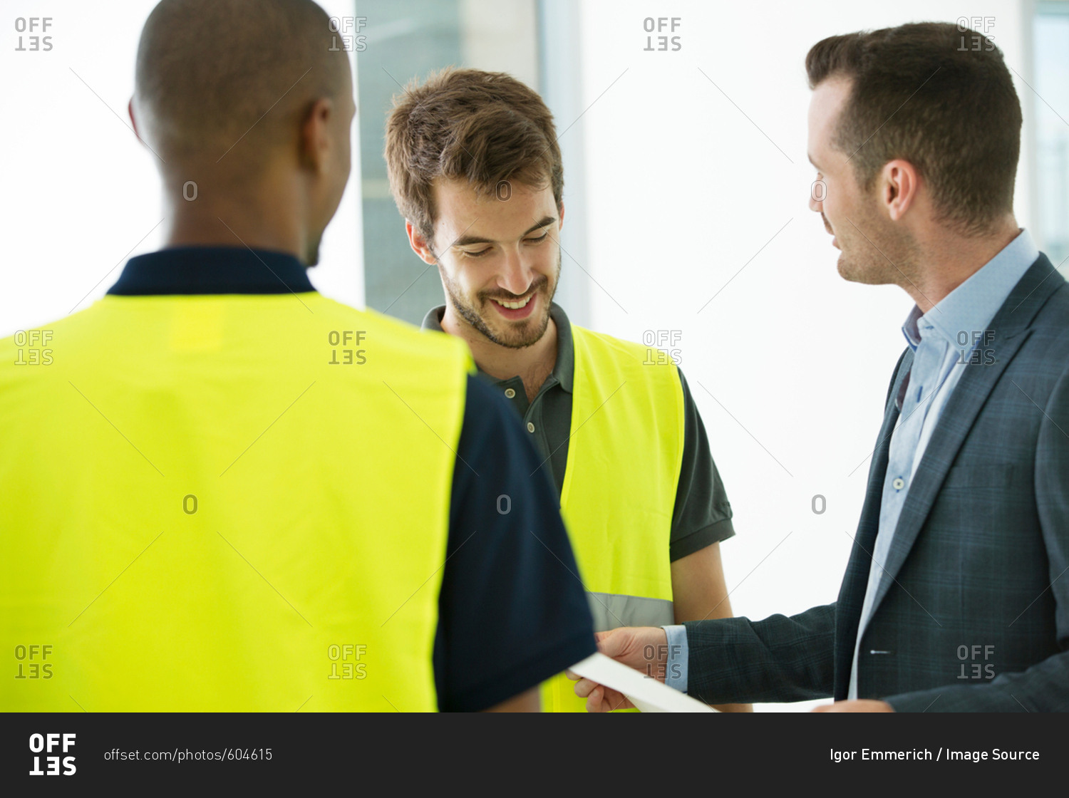 Two men wearing hi vis vests, having discussion with businessman