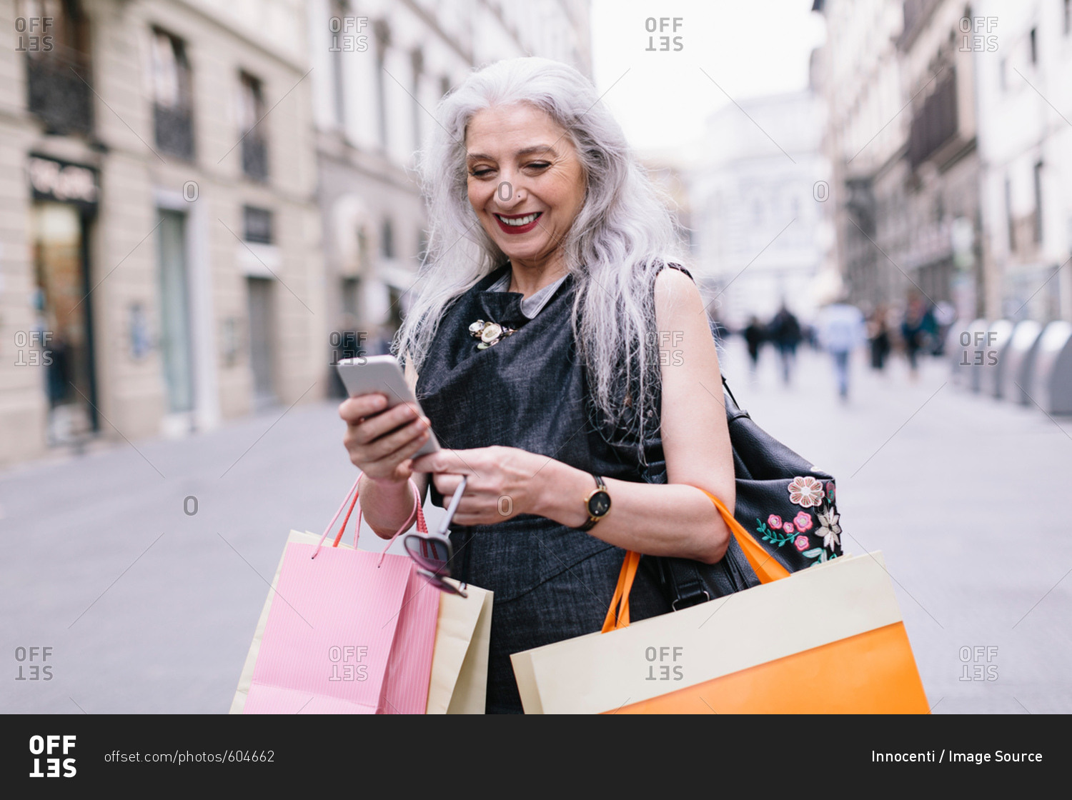 Stylish mature female shopper looking at smartphone on street, Florence, Italy