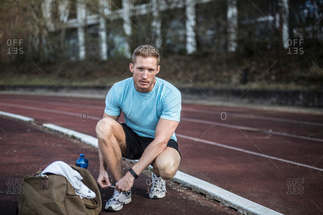 Young man crouching beside sports track, tying shoelaces