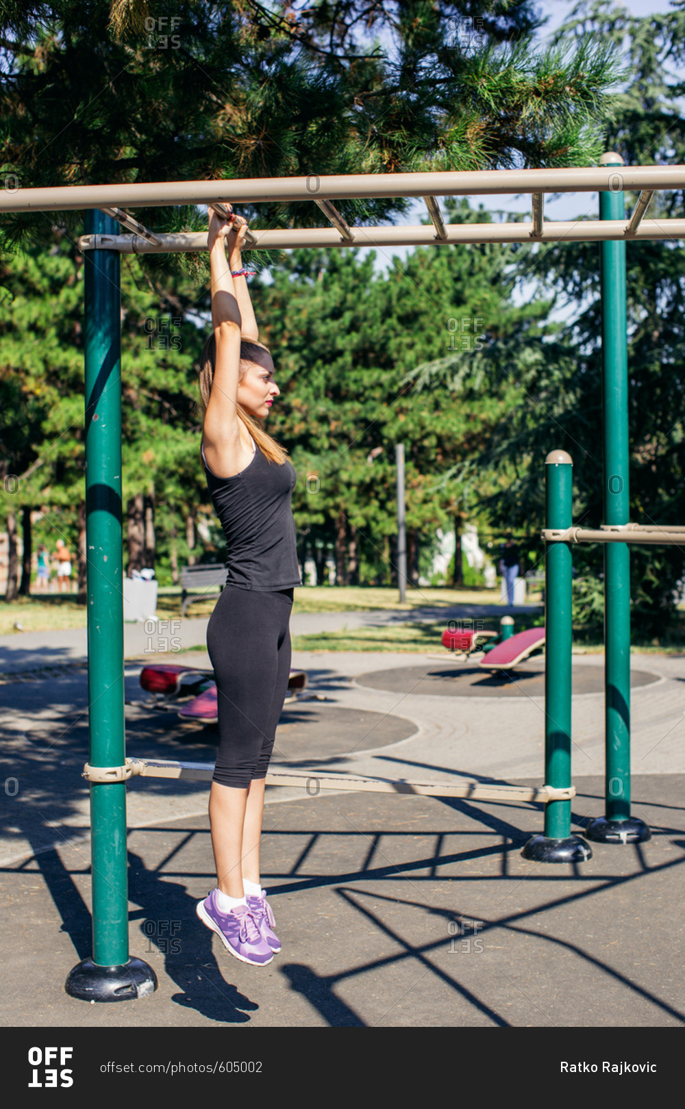 Woman hanging from monkey bars in outdoor workout stock photo OFFSET