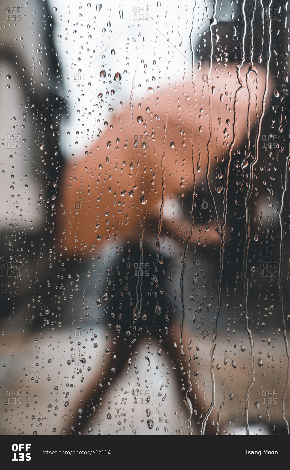 View through rain covered window of person walking with umbrella