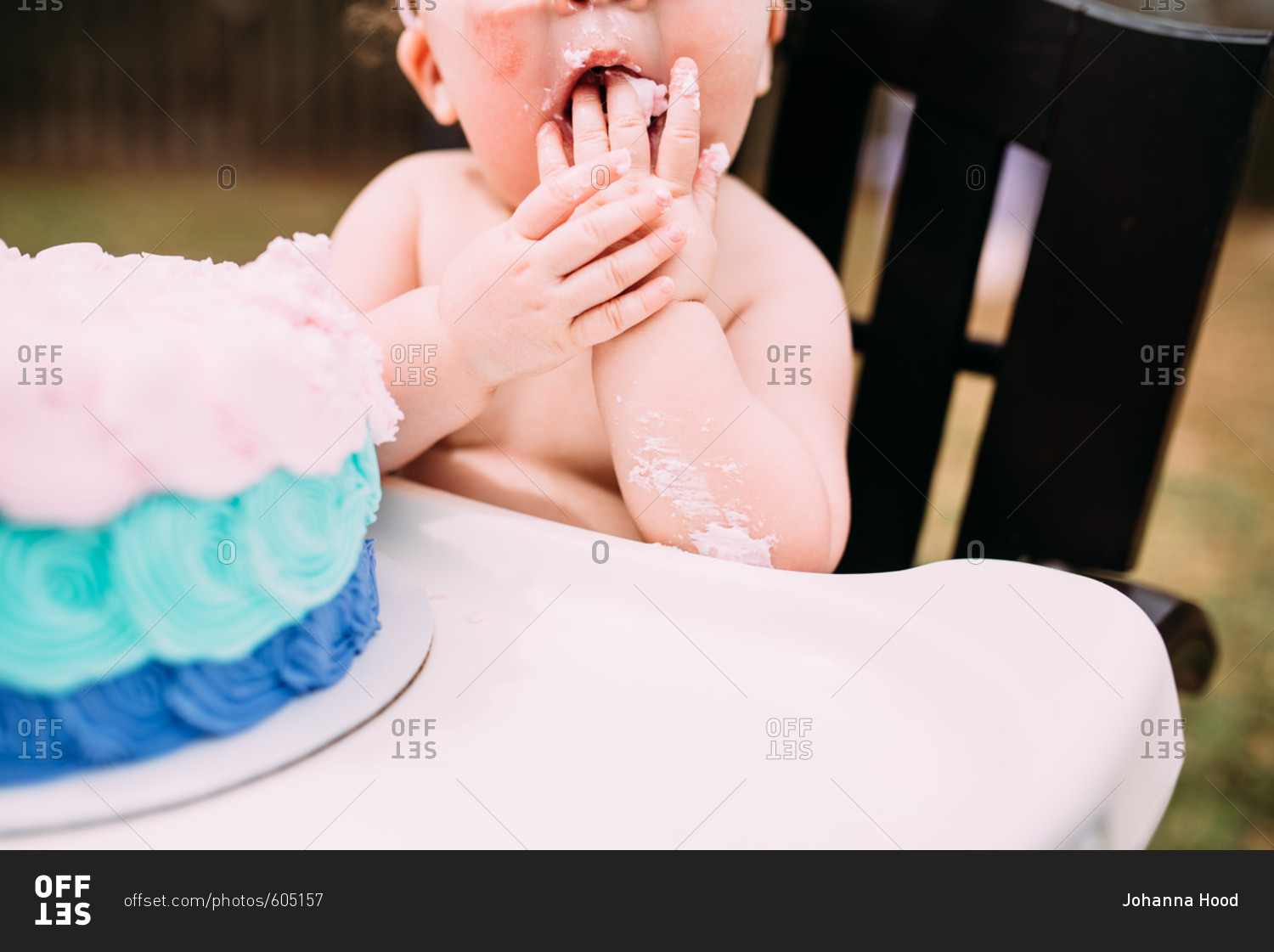 Little baby making mess while eating birthday cake outdoors