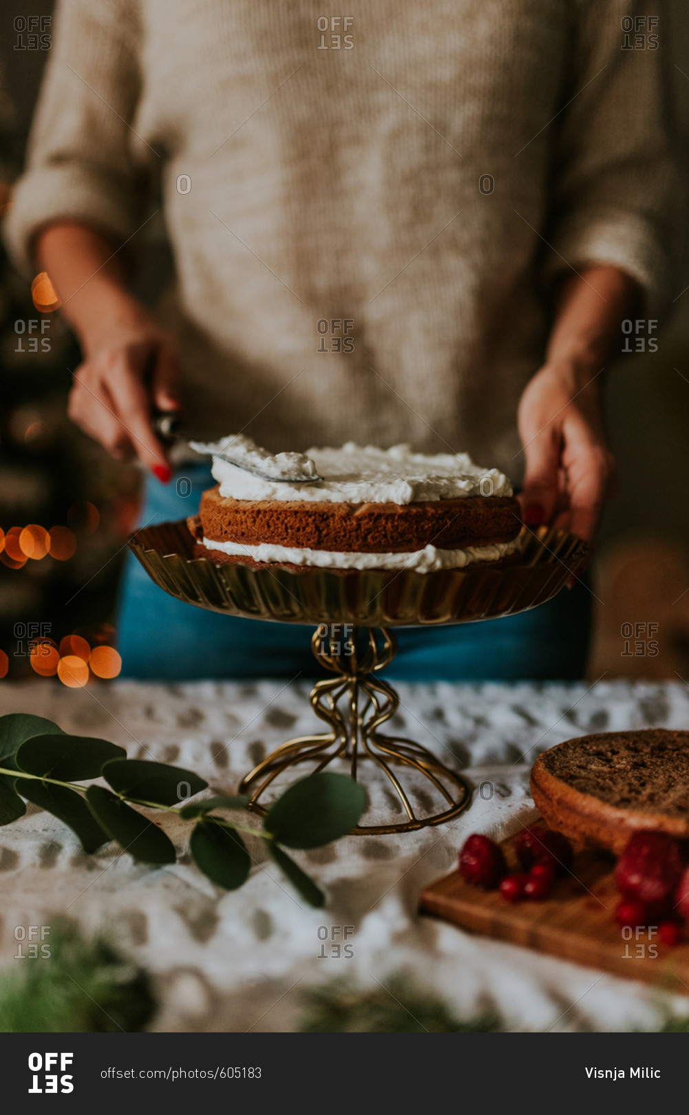 Woman putting cream on cake panes making naked cake with blurred Christmas tree in the background
