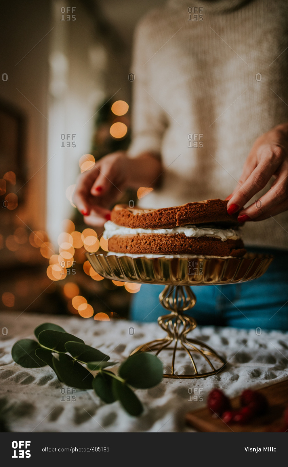 Woman putting layers of cake panes and making winter inspired naked cake with Christmas tree in the background