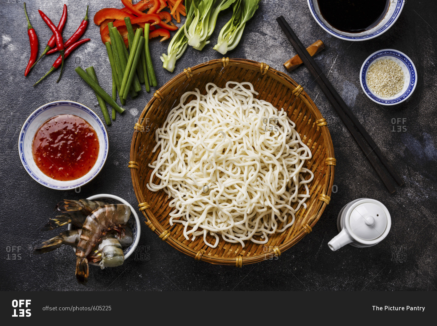 Raw Udon noodles in bamboo basket and Ingredients for cooking asian food with Tiger shrimps, greens, vegetables, spices on dark background