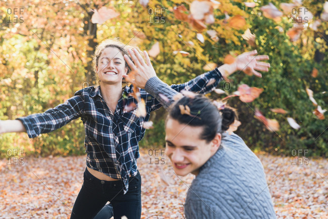 Happy playful young woman throwing autumn leaves on man in forest