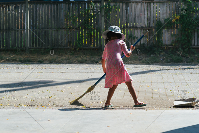 Little girl sweeping leaves on a patio