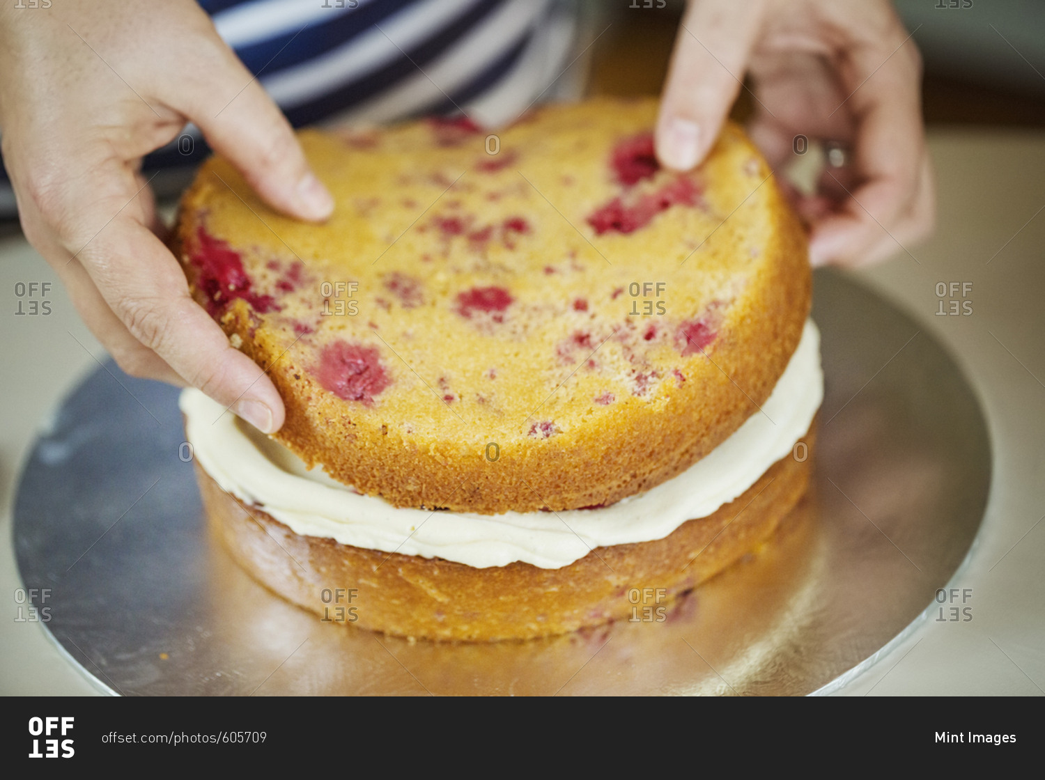 Close up high angle view of person assembling a layer cake, placing top on layer of cream.