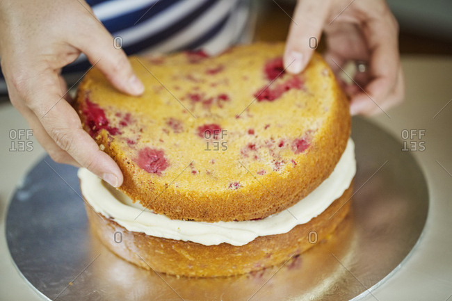 Close up high angle view of person assembling a layer cake, placing top on layer of cream.