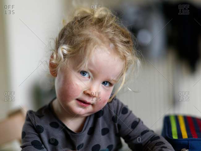 A portrait of a smiling young blonde girl with blue eyes at home with a short depth of field and blurred background