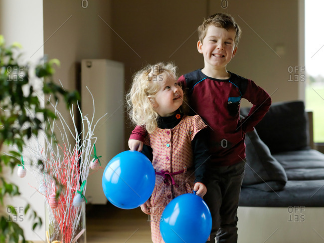 Two kids, brother and sister posing and having fun with blue birthday balloon at home with a short depth of field