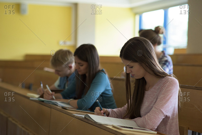 Young College Students Writing On Book At Desk While Sitting