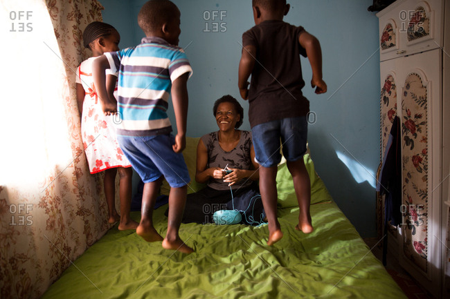 Three children jumping on bed whilst mother crochets