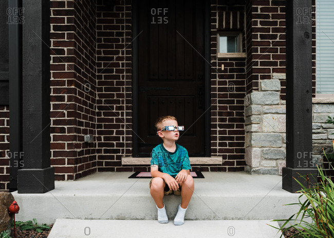 Boy sitting on front step in eclipse glasses
