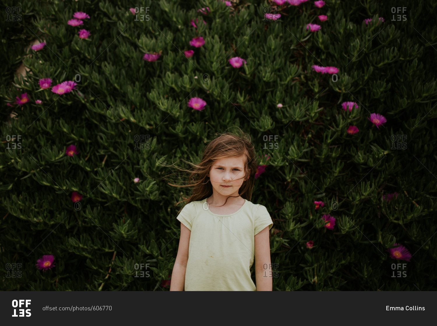 Young girl standing in front of bush with pink flowers