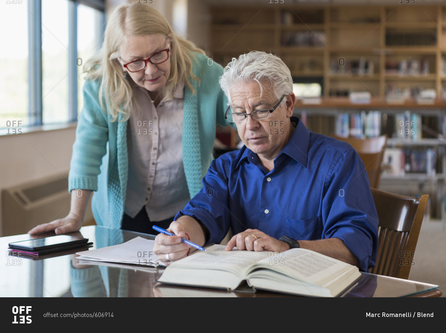 Older woman helping man reading book in library