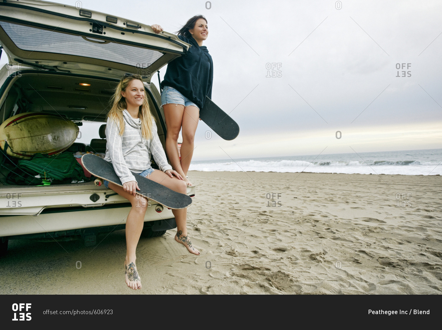 Caucasian women in car hatch at beach holding skateboards