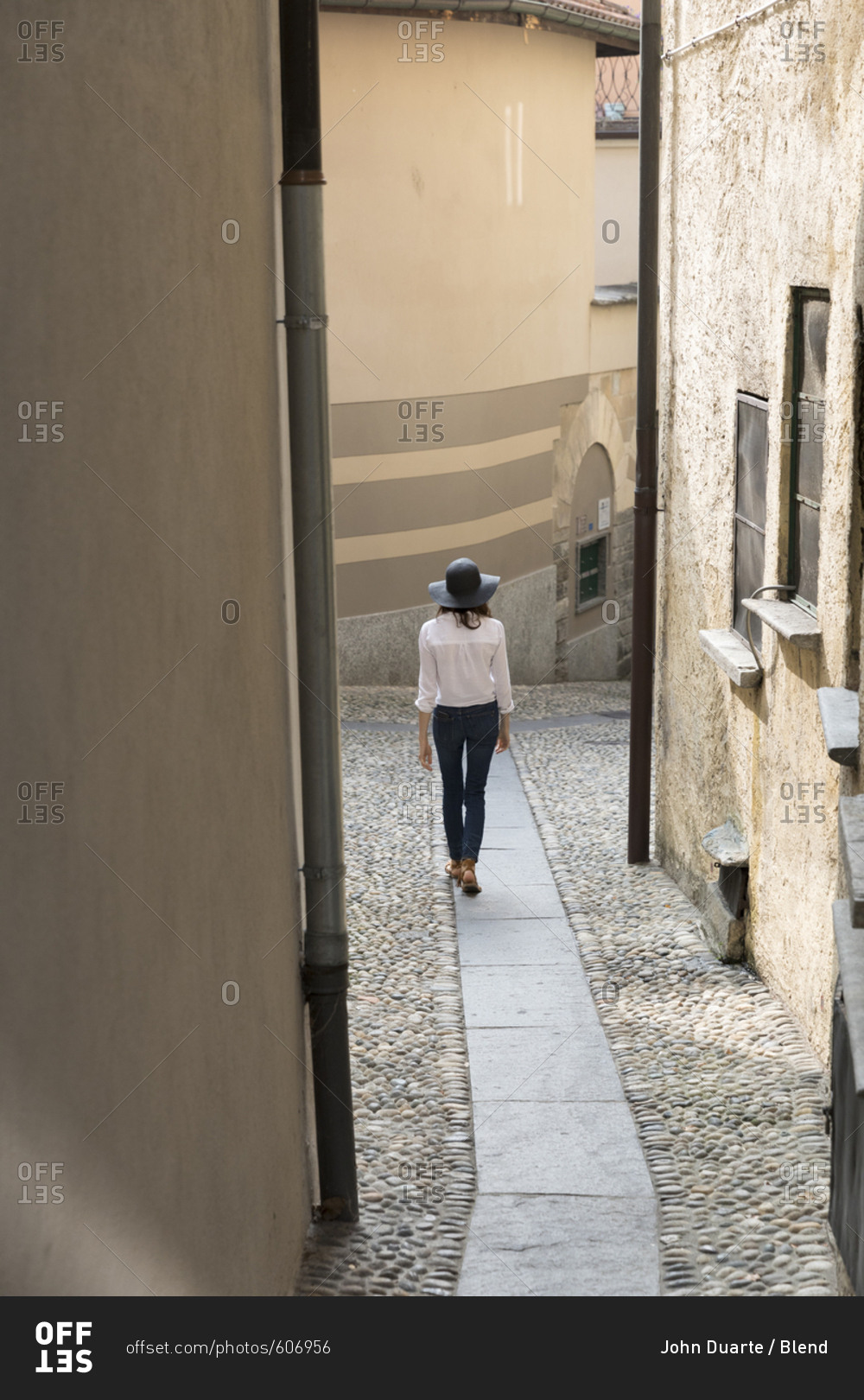 Woman wearing sun hat walking on narrow sidewalk