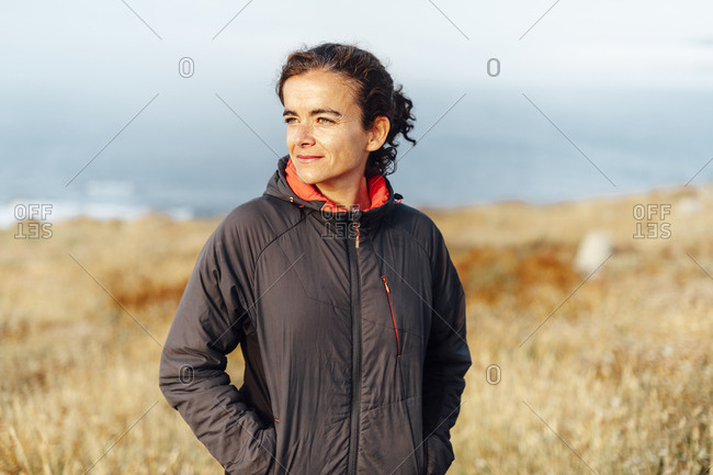 Mid aged woman looking at horizon on a windy day wearing a grey jacket