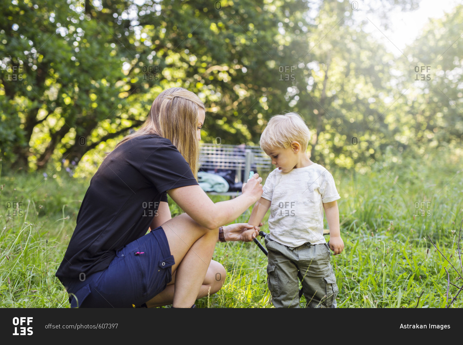 Mother spraying son (2-3) with insect repellant