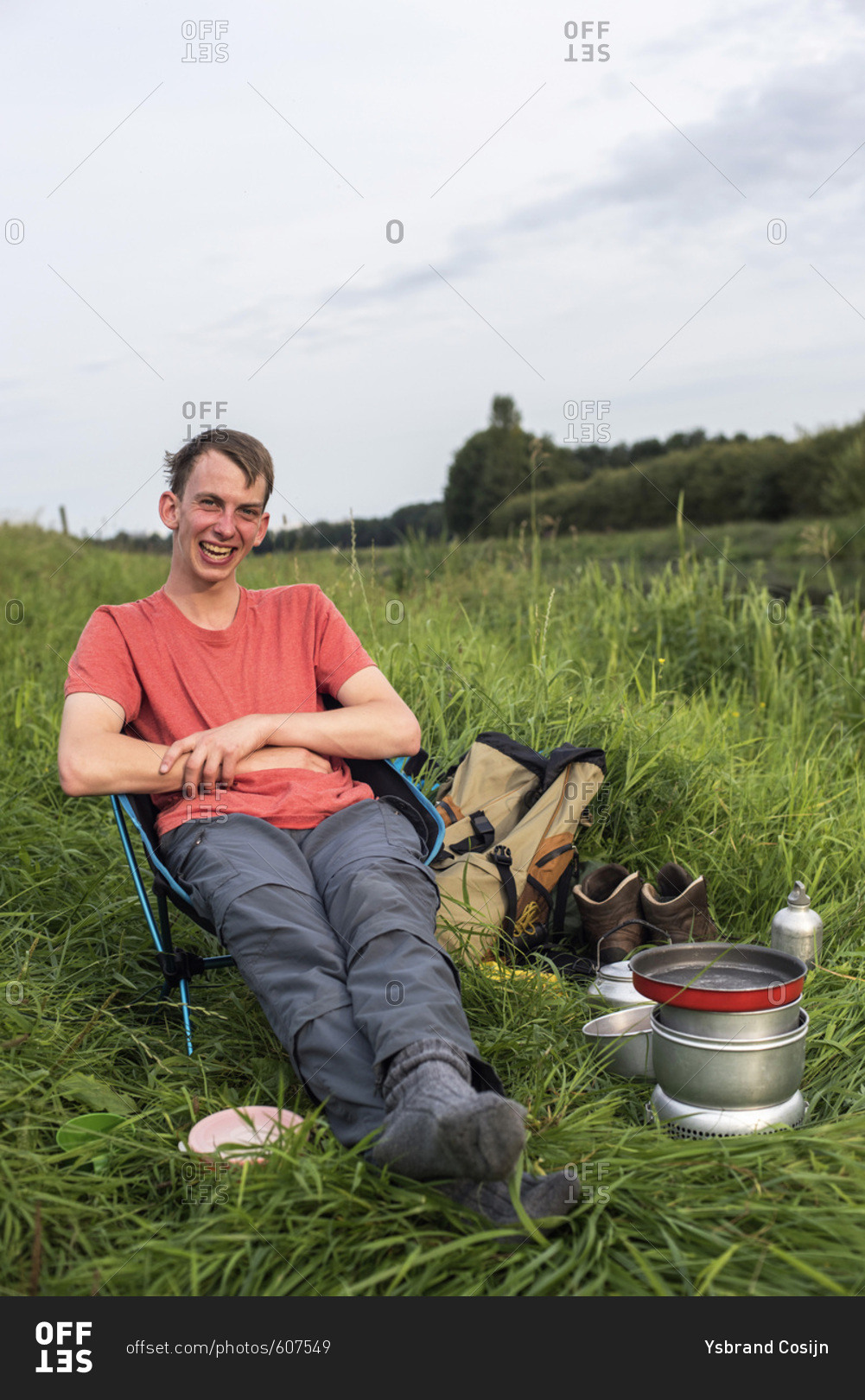 Happy young man sitting in chair with camping stove in field